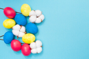 Easter composition. Colored eggs blue, yellow and red on a blue background. Copy space. Place for text. Flat lay. Top view. Preparation for the holiday. Cotton flowers