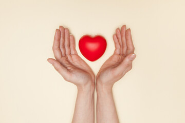 Health, medicine and charity concept - close up of female hands with small red heart