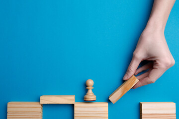 Woman building bridge with wooden blocks on light blue background, top view. Connection and risks concept