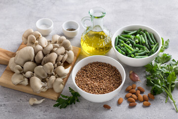 Ingredients for a vegetable vegan dish: buckwheat, oyster mushrooms, green beans, almonds, olive oil, parsley, garlic and spices on a gray background, top view