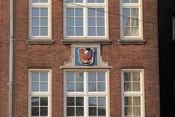 Fototapeta na wymiar Amsterdam Damrak Street Brick Building Close Up with Stone Tablet Depicting a Hand Holding a Red Chicken, Netherlands