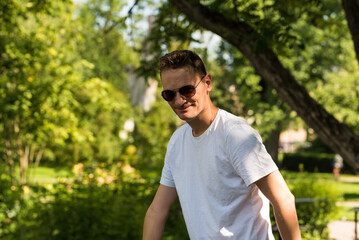 Fototapeta na wymiar Attractive fourty year old man with sunglasses and white T-shirt posing in the botanical garden