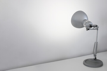 Silberne Schreibtischlampe strahlt weiße Wand auf Schreibtisch an - minimalistischer Arbeitsplatz...