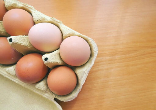 Colorful Organic Chicken Eggs In A Carton Pack Over A Wooden Table. Fresh Product, Local Farm, Sustainable And Healthy Lifestyle. View From Above. 