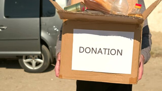 Volunteer man carrying the cardboard box with the food and drink for refugees people remaining in the street.