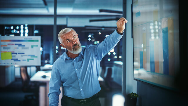 Company Operations Director Holds Sales Meeting Presentation For Employees And Executives. Creative White Entrepreneur Uses TV Screen With Growth Analysis, Charts, Ad Revenue. Work In Business Office.