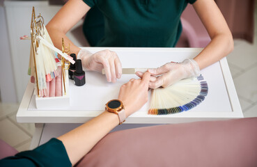 Fototapeta na wymiar Crop view of manicure specialist filing woman nails with nail file. Female manicurist in sterile gloves doing manicure for client in beauty salon.