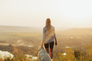 Young woman and dog admiring sunset and beautiful landscape in the mountain.