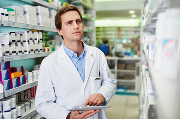Digitizing drug store management duties. Shot of a young pharmacist using a digital tablet in a...