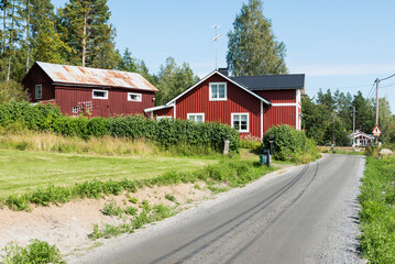 Fototapeta na wymiar Borka, Gavleborgs Lan, Sweden - Countryroad towards the village with typical Swedish summerhouses in red wood
