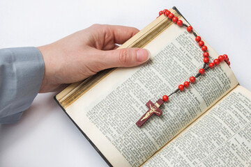 A woman reads an old, shabby bible in German, on the book lies a holy red rosary