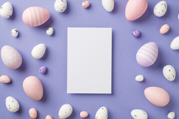 Top view of big vertical white post card and many multicolored Easter eggs different size on the pastel violet isolated empty background in the middle