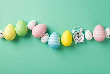 Top view photo of easter decorations row of multicolored easter eggs and white alarm clock on isolated teal background with copyspace