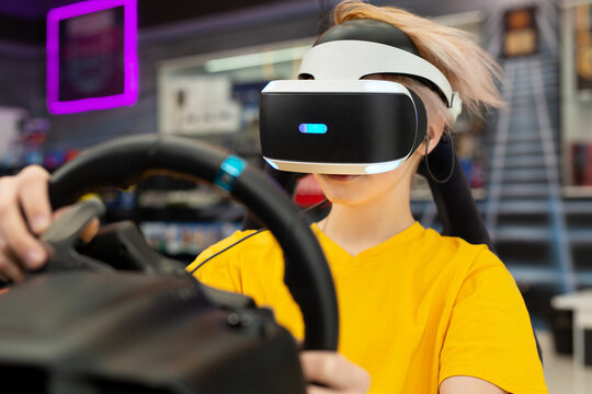 Teenage boy wearing virtual reality glasses, who holds on to the steering wheel and plays a computer game on the console