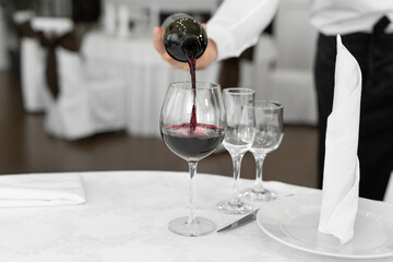 Male waiter in white gloves pours red wine into a glass.