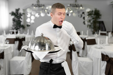 Male waiter in a rstoran with a dish in his hands shows that this dish is tasteless.