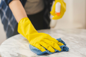 Cleaning hygiene, close up hand of maid, waitress woman wearing yellow protective gloves while cleaning on wood table, use blue rag wiping to dust and spray in restaurant. Housekeeping cleanup,cleaner