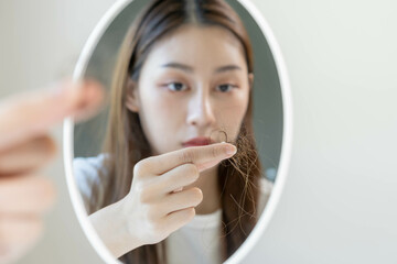 Damaged hair, face worried asian young woman, girl look into mirror, holding hair loss and show...