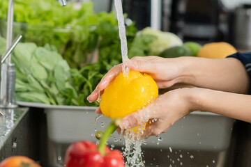 Close up asian young housekeeper woman,  washing sweet pepper, yellow paprika, vegetables with...
