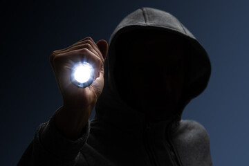 Hooded burglar. Silhouette of thief and flashlight - obrazy, fototapety, plakaty