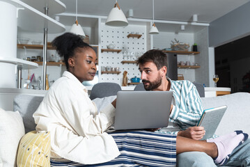 Young couple small business owners working from home. Married man and woman sitting on sofa in apartment work on new commercial ideas and strategy for web site and company they own.