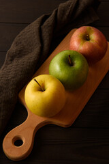 Yellow, green and pink apples lie on a wooden board next to a brown cotton napkin on a brown wooden background.