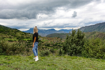 Naklejka premium A girl on the background of the village of Kurib in the Caucasus mountains, on top of a cliff. Dagestan Russia June 2021