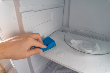 Defrosting and cleaning the freezer. A man wipes meltwater with a sponge. Shallow depth of field. Space for text.