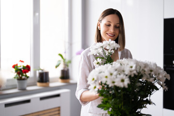 Happy and joyful young woman in white arranging white flowers at home in the kitchen