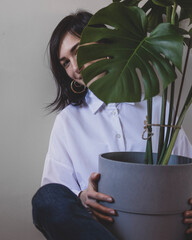 Young woman is sitting with a big flower pot with monstera © Yurii Kushniruk