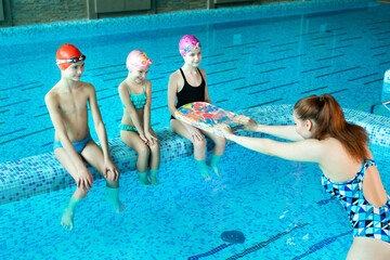 Female instructor teaches a group of children to swim in an indoor pool.