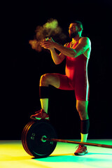 One young man, professional weightlifter sportswear training with barbell isolated dark background...