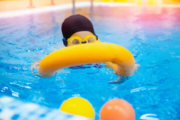Little kid girl with glasses learning to swim with pool yellow noodle. Concept training swimming child