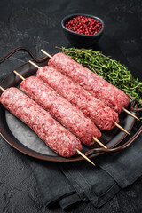 Raw Turkish Urfa kebab  skewers in steel tray with herbs. Black background. Top view