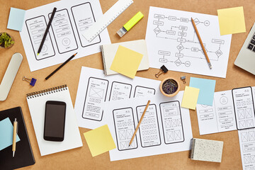 Top view image of busy web UX designers workspace with many mobile app wireframe sketches and user flow. 