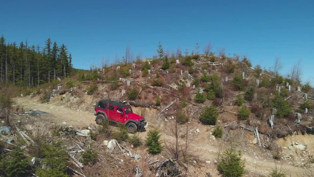 red jeep 4x4 off road vehicle driving on remote logging road deep within forest on mountain surrounded by green trees beautiful Aerial reverse revealing dirt road ahead jeep mountains blue sky scenery