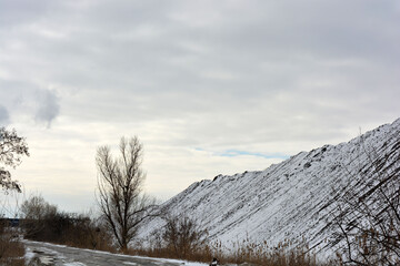 Bright, colorful high mountains, peaks, steep hills are located along the road and covered with light white snow in winter. A very interesting and bewitching landscape against a gray-white sky. 