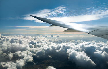 Wing of an airplane flying over morning clouds. View on cloud and blue sky through the airplane window.