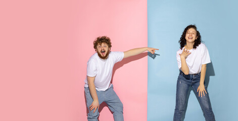 Excited couple of young funny and happy man and girl laughing studio on blue and pink trendy color background.
