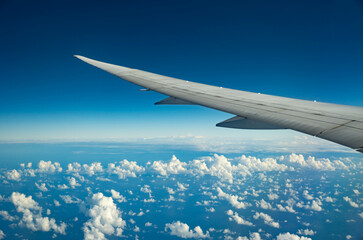 Wing of an airplane flying over morning clouds. View on cloud and blue sky through the airplane window.