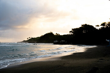 Sunrise over tropical beach, mountain and palm trees. Beautiful view in Dominican Republic. Cloudy sky and golden rays of sun. 