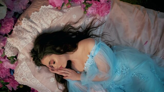 Sleeping fairy beauty girl princess. Fantasy woman goddess lies on medieval bed in sleep. Blue vintage dress. Backdrop pink white peony flowers green garden bedroom nature. Tranquility harmony concept