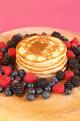 Pancakes with red fruits: blueberries, raspberries and blackberries on a colorful  background 