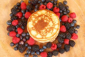 Pancakes with red fruits: blueberries, raspberries and blackberries on a colorful  background 