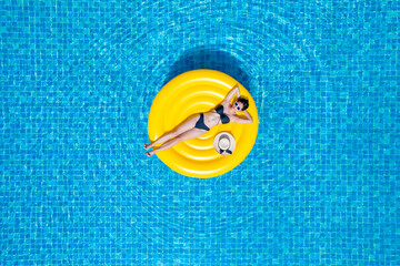 Top view of young asian woman in bikini on the yellow inflatable ring in the pool at private villa....