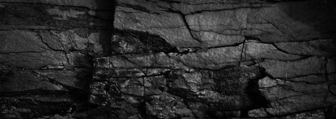 Black and white rock texture. Crushed mountain surface. Close-up. Grunge backdrop. Dark gray stone background with space for design. Wide banner. Panoramic.