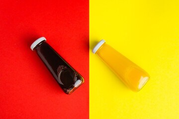 Bottles with yellow and red liquid halthy beverage on yellow and red background. Orange cherry juice