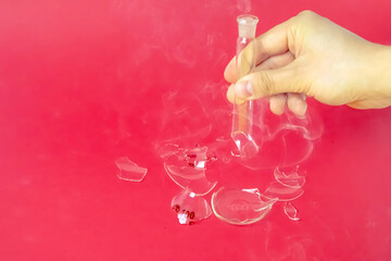 Hand holding broken laboratory glass flask smoking on red background. Lab experiment.