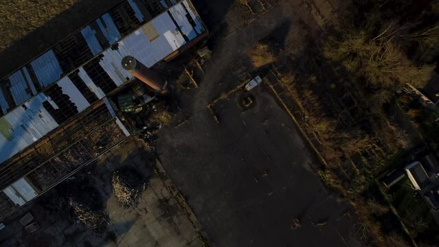 Old factory with broken rooftop and abandoned surroundings, aerial top down ascend view