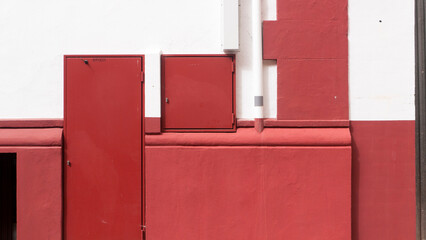 Fachada callejera blanca y roja con tapas metálicas de caja de suministro electrico